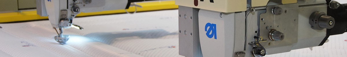 Cabezal de máquina de costura industrial realizando un acolchado de precisión con hilo sobre tejido técnico blanco.